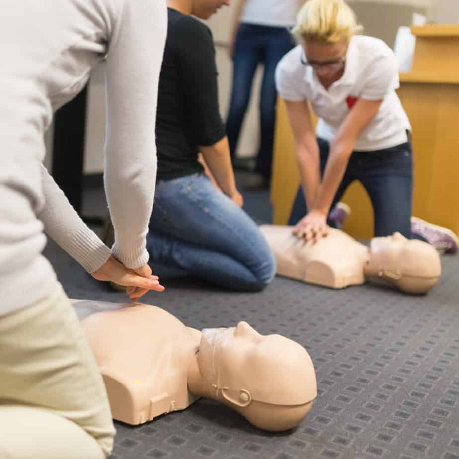 A group of adult students practicing CPR chest compressions on a training dummy.