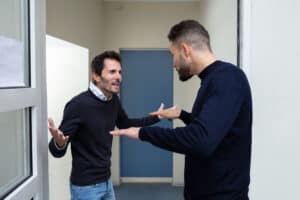 Two Young Men Standing At The Door Entrance Quarreling With Each Other